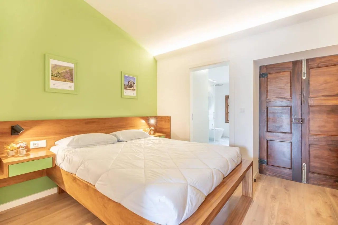 Segundo quarto de casal com parede verde e porta em madeira maciça