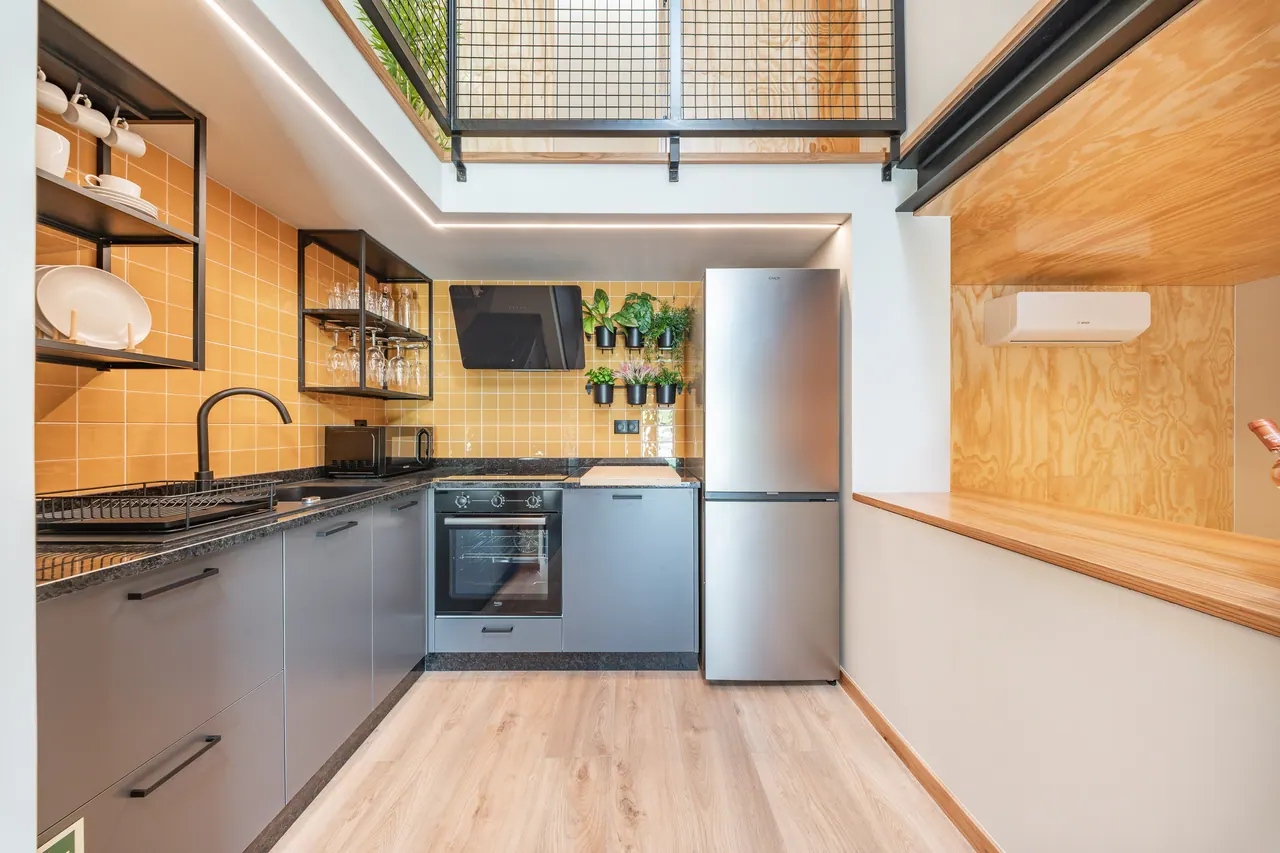 Cozinha equipada em madeira clara com frigorífico e placa de indução