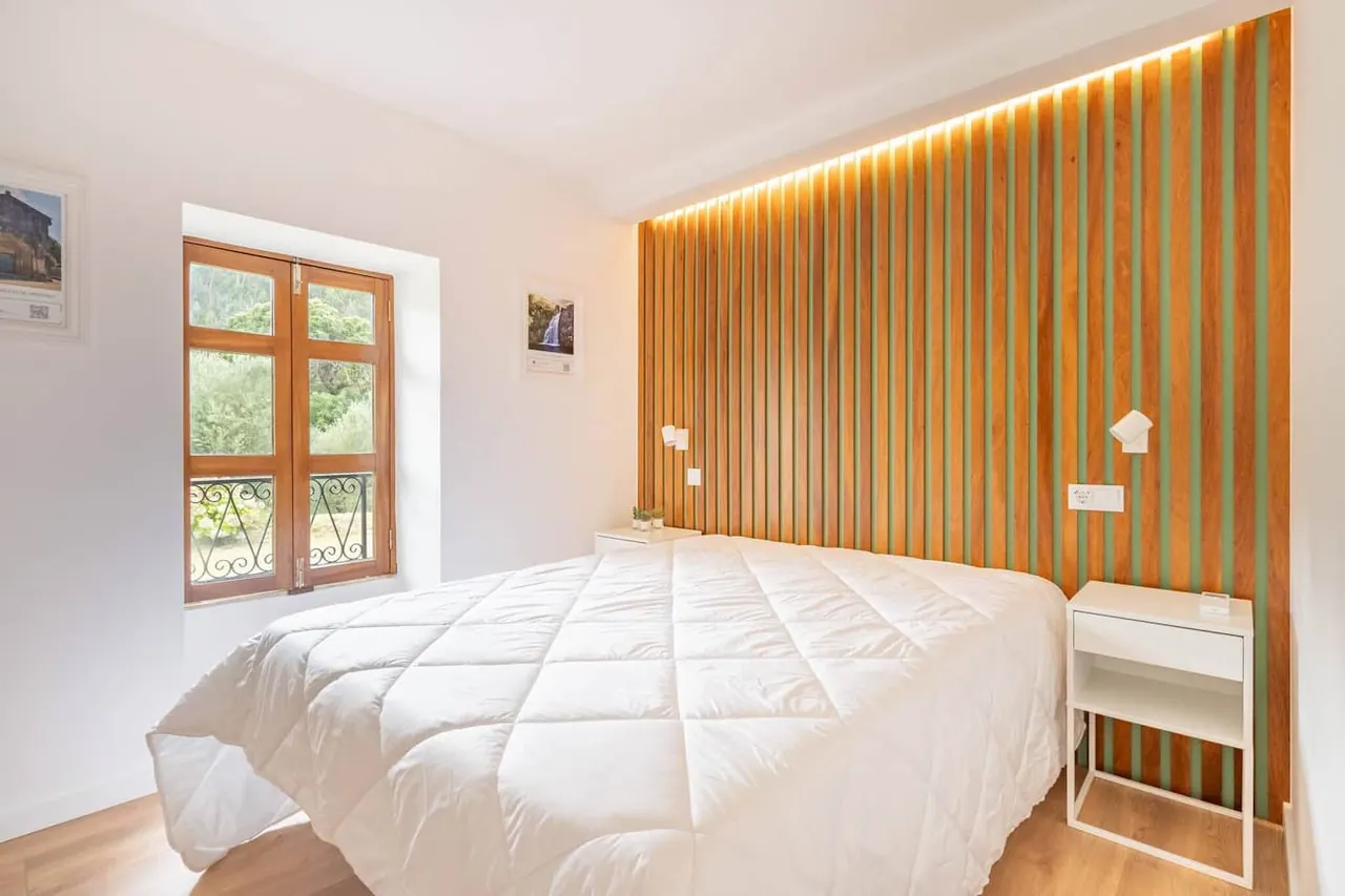 Quarto de casal com cabeceira em madeira ripada e janela para o jardim